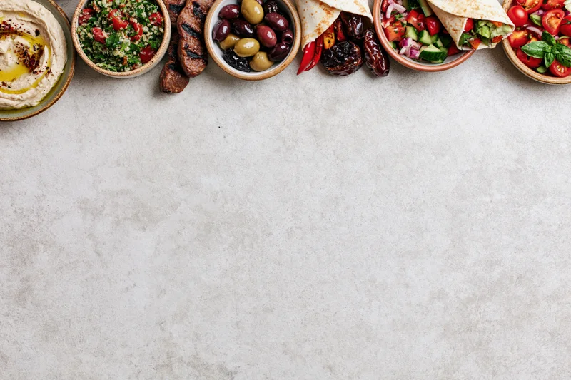 Middle eastern mezze spread arranged along the top edge of a white stone countertop with copyspace below