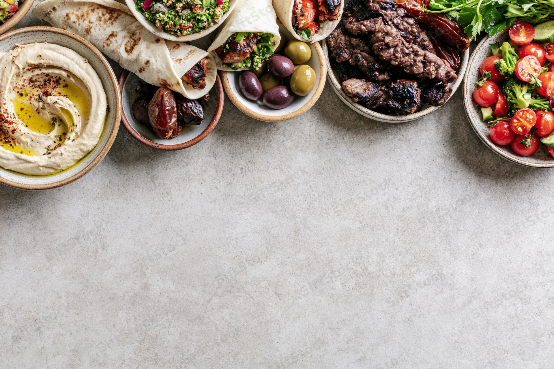 Middle eastern mezze spread arranged along the top edge of a gray stone countertop with copyspace below