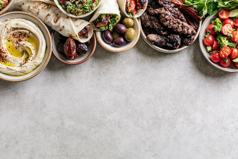 Middle eastern mezze spread arranged along the top edge of a gray stone countertop with copyspace below