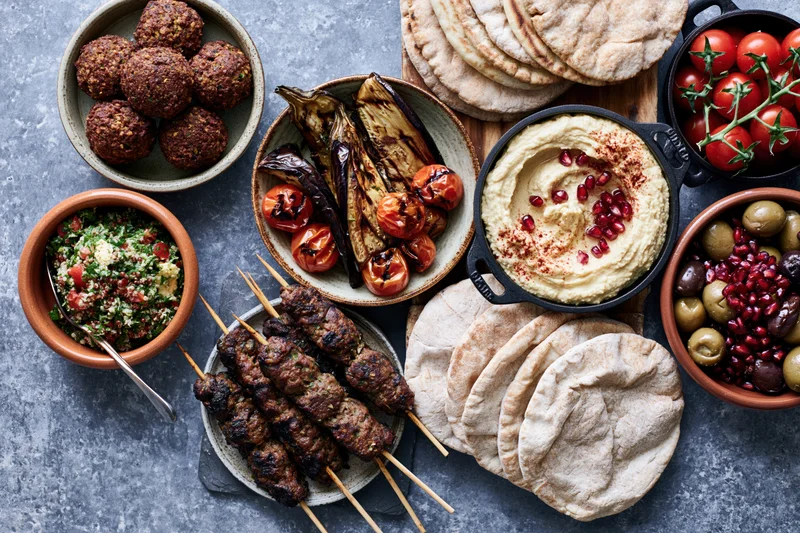 Middle eastern mezze spread with hummus, falafel, kebabs and pita arranged on a table overhead