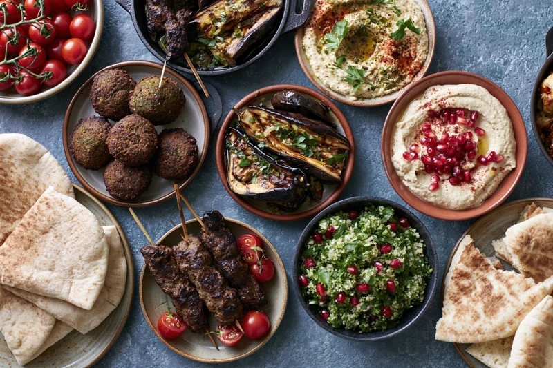 Middle eastern mezze spread with hummus, falafel, kebabs and pita on a table viewed from above