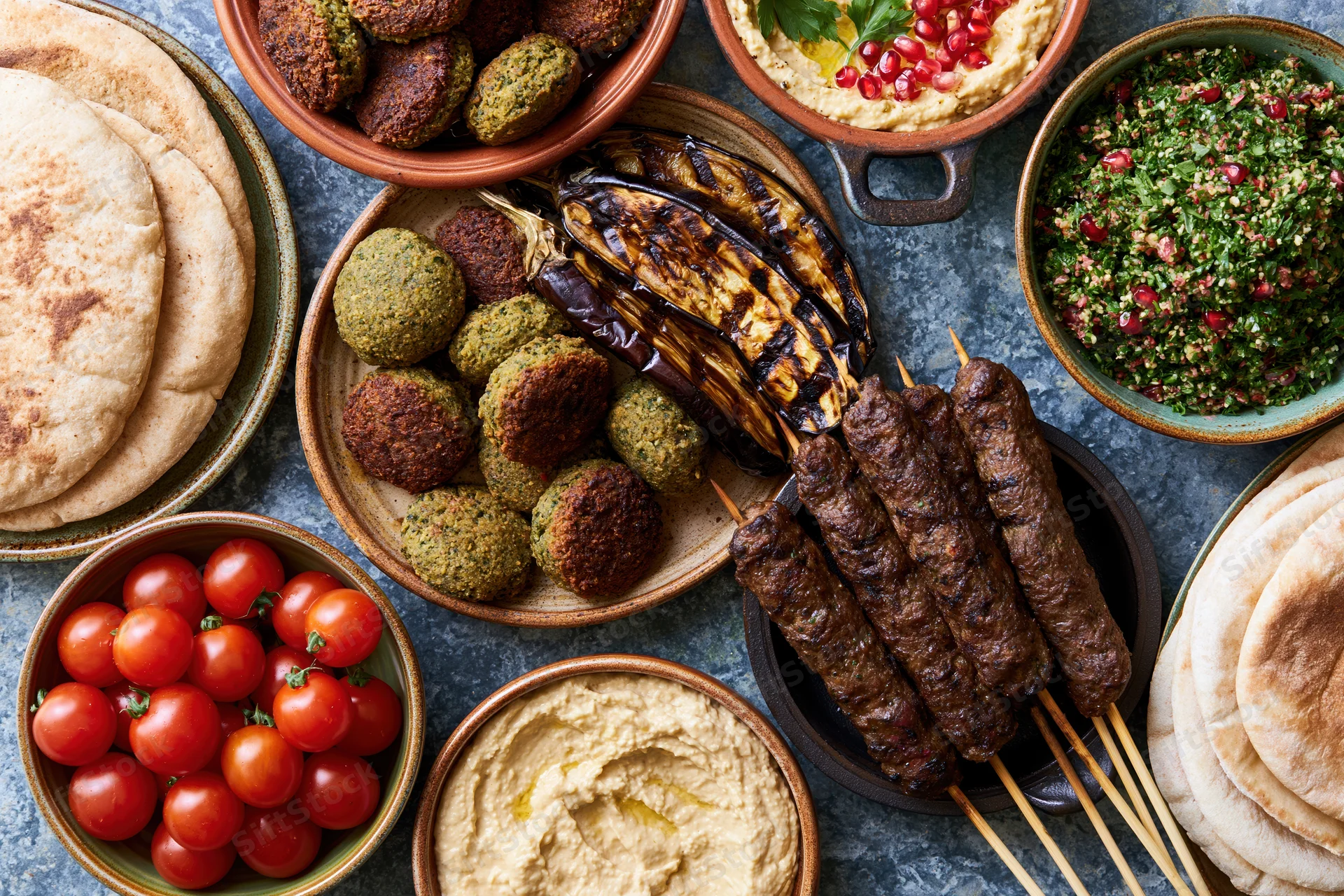 Middle eastern mezze spread with hummus, falafel, kebabs and pita on a stone table viewed from above
