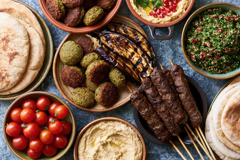 Middle eastern mezze spread with hummus, falafel, kebabs and pita on a stone table viewed from above
