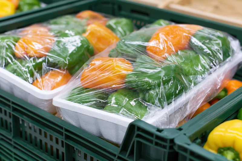Green and orange peppers in plastic-wrapped foam trays inside green crates at a grocery store