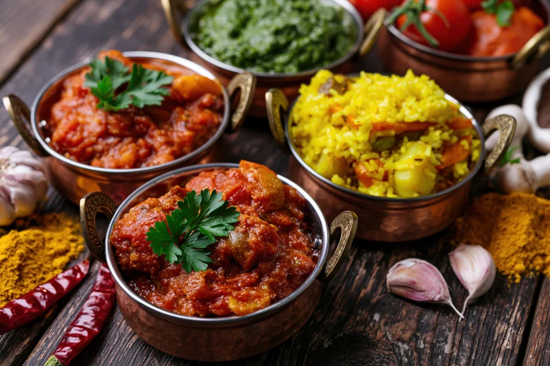Multiple indian dishes served in traditional copper karahi bowls on wooden table