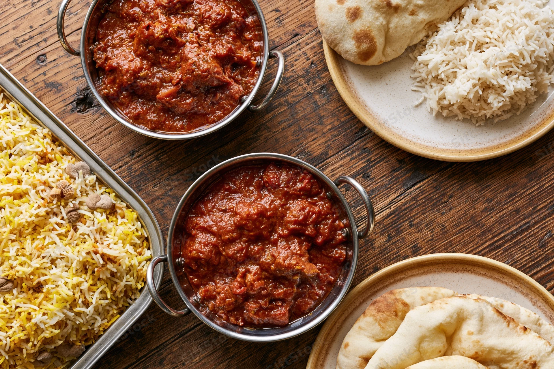 Indian curry and biryani dishes served with naan bread on a rustic wooden table