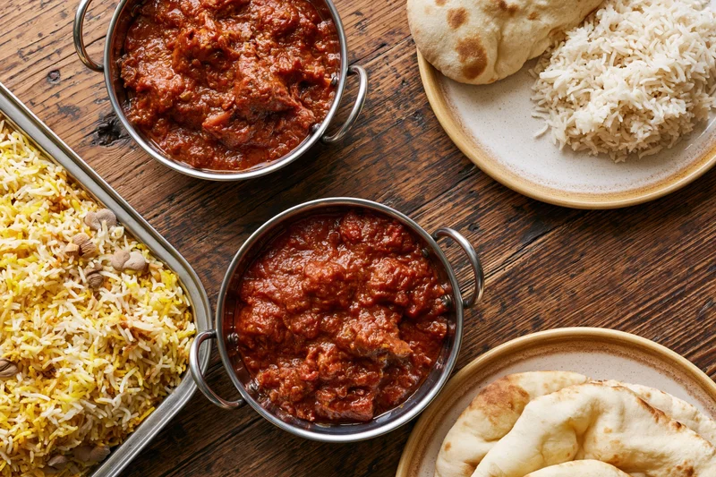 Indian curry and biryani dishes served with naan bread on a rustic wooden table