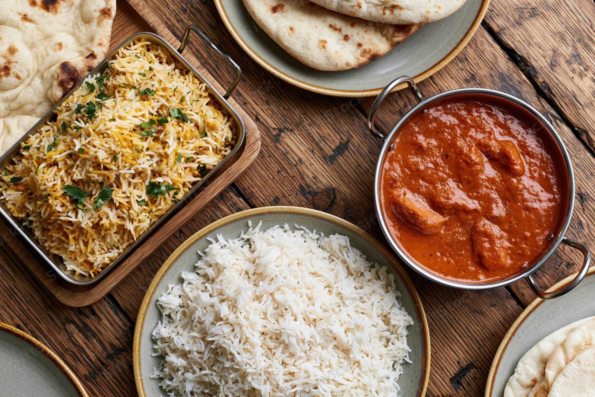 Indian dishes including curry, biryani, and naan arranged on a rustic wooden table