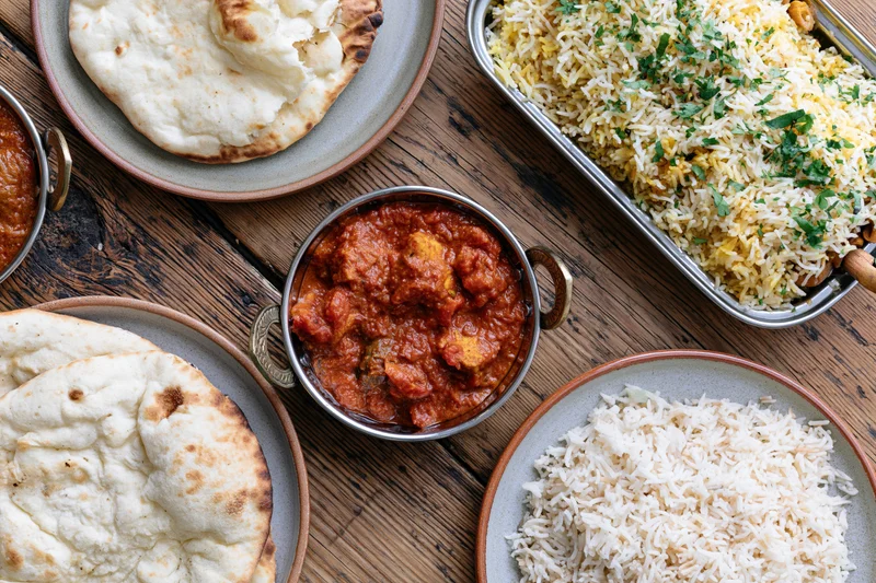 Indian dishes including curry, biryani, and naan arranged on a rustic wooden table