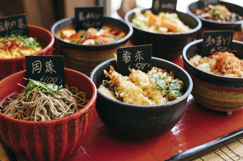 Multiple japanese food bowls with price signs arranged on a red lacquered tray