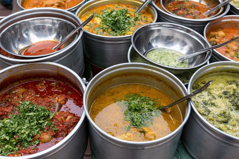 Multiple aluminum pots filled with colorful thai curries and sauces arranged for serving at a street food market