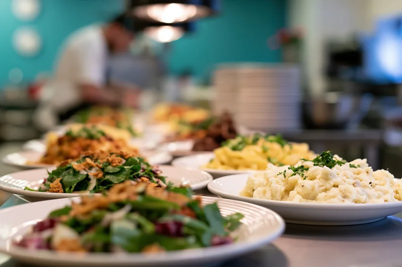 Multiple plated dishes lined up on a restaurant pass counter with a chef working in the background