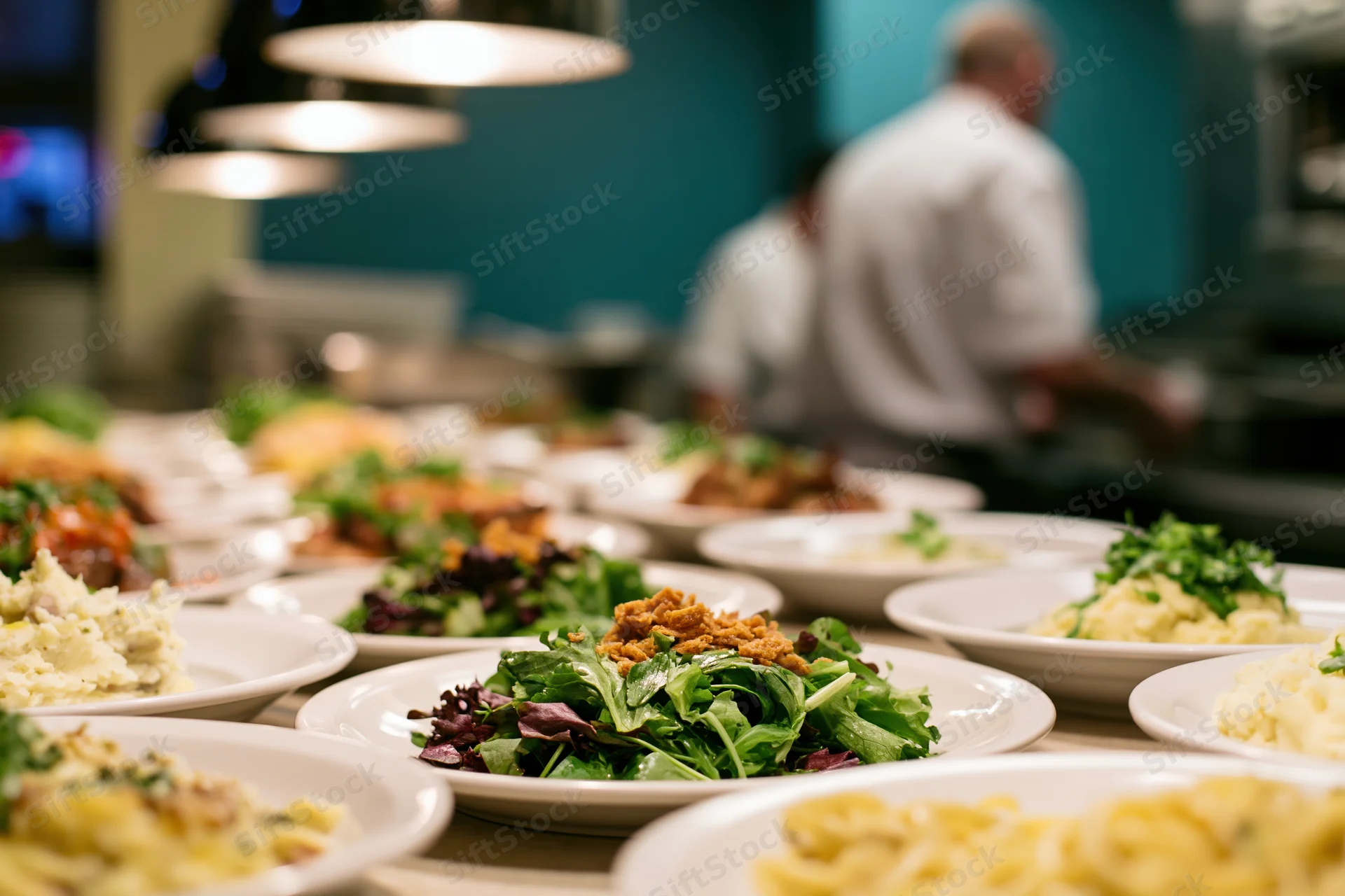 Multiple plated dishes arranged on a restaurant pass counter with chefs working in the background