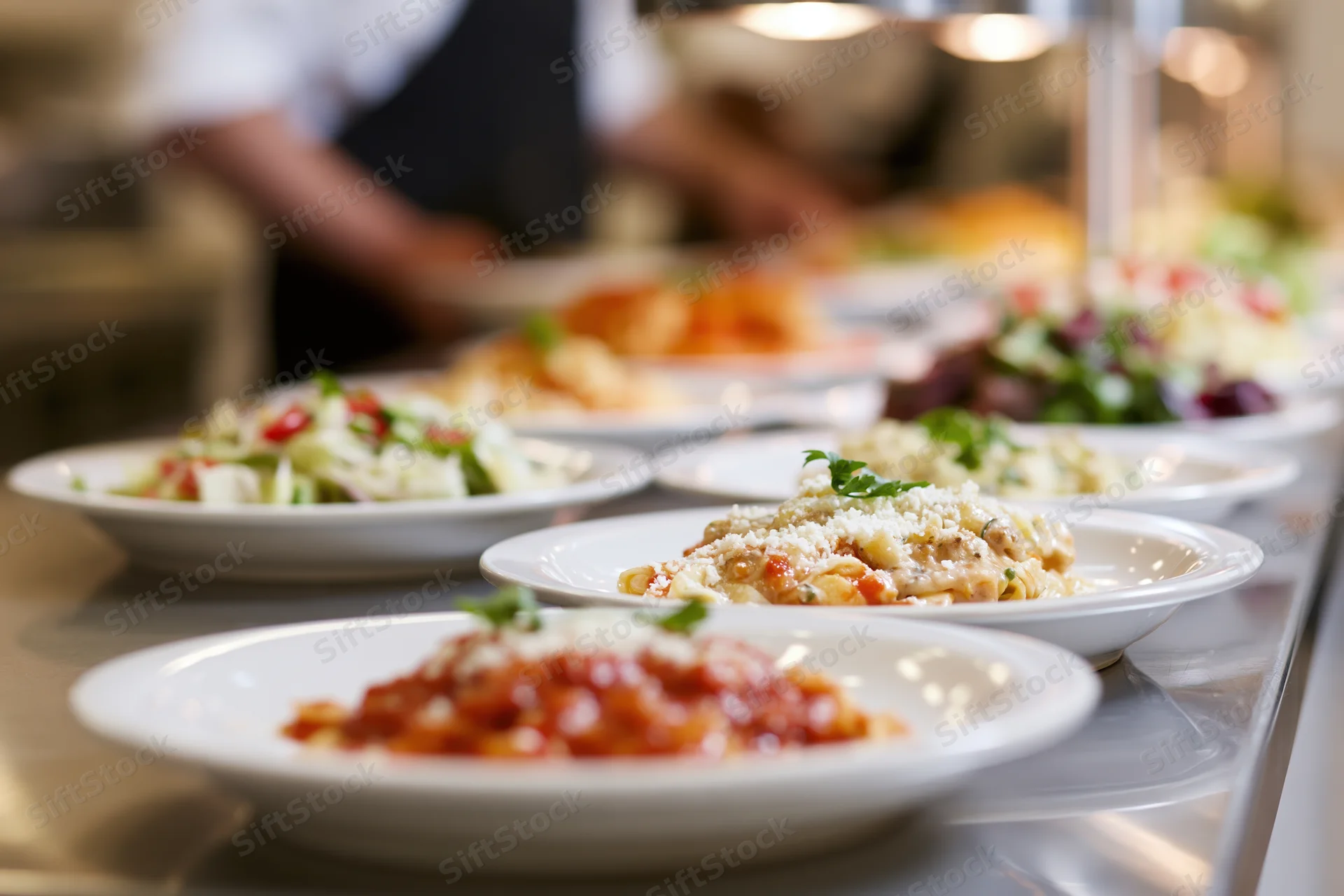 Multiple plated dishes arranged in a row on a stainless steel buffet counter in a restaurant kitchen