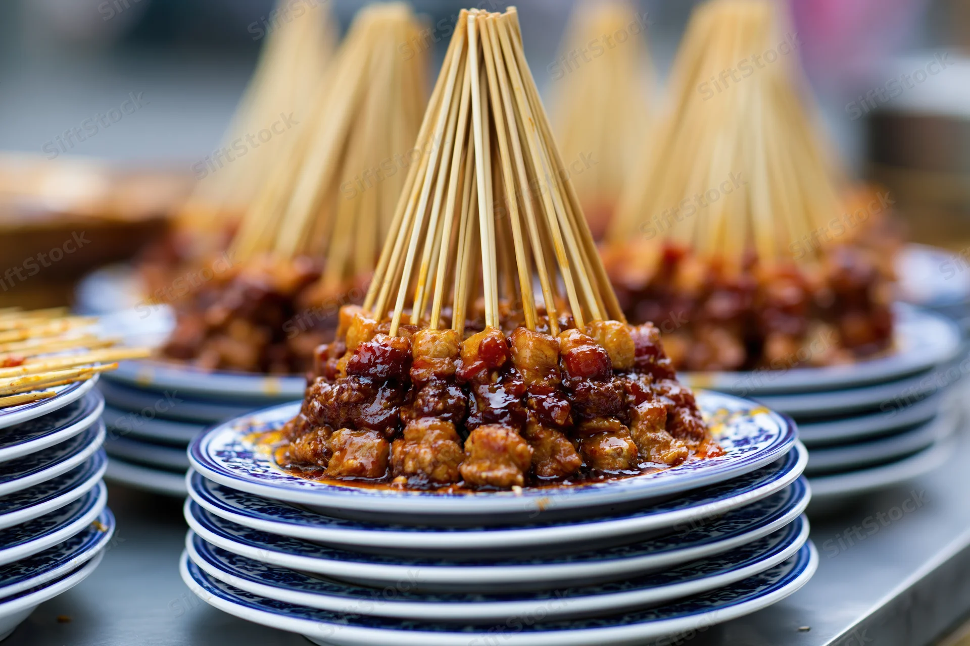 Stacked plates of meat skewers with glossy sauce arranged on a metal tray at a street food stall
