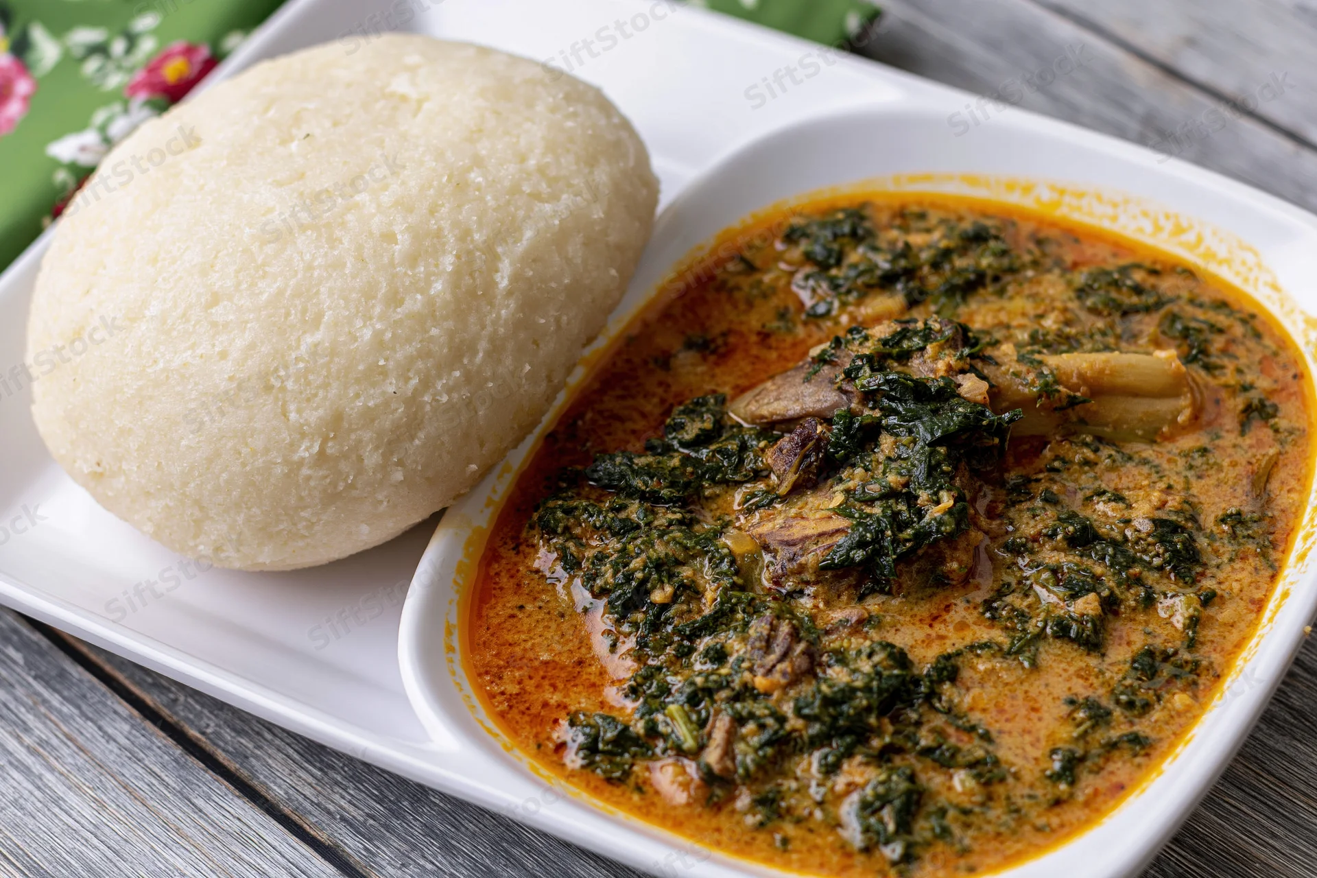 Eba cassava fufu ball served alongside egusi vegetable stew on a white plate on a wooden table