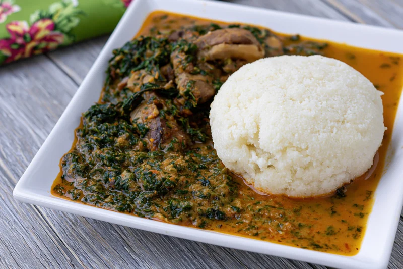 Eba cassava fufu ball served with egusi vegetable stew on a white square plate