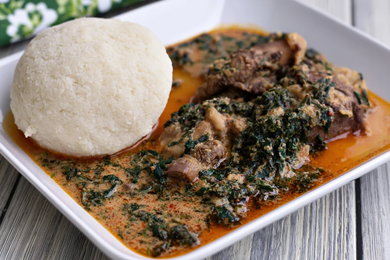 Eba cassava fufu ball served with egusi vegetable stew on a white square plate