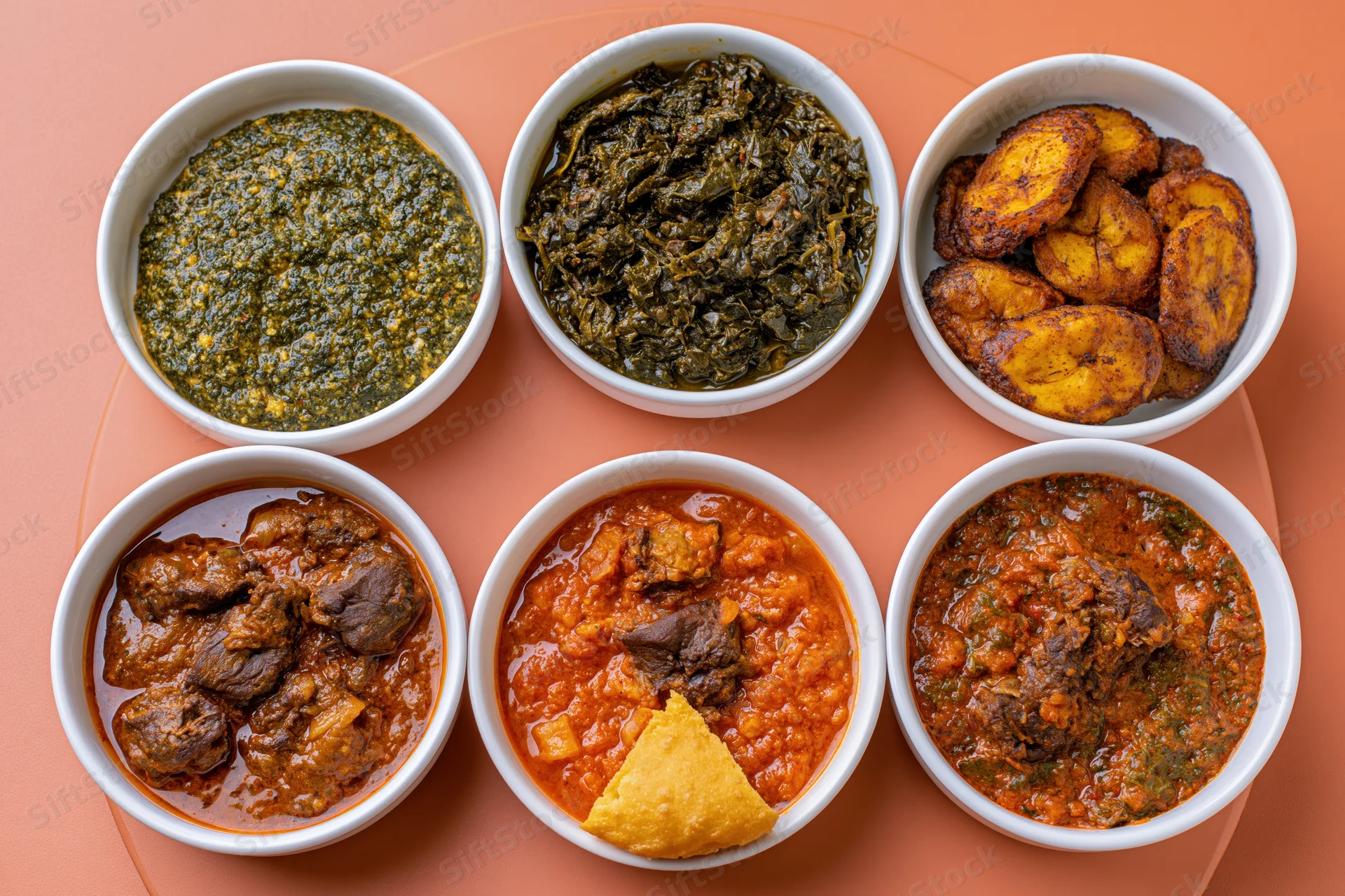 Six white bowls of african stews and vegetables arranged in a circle on an orange surface