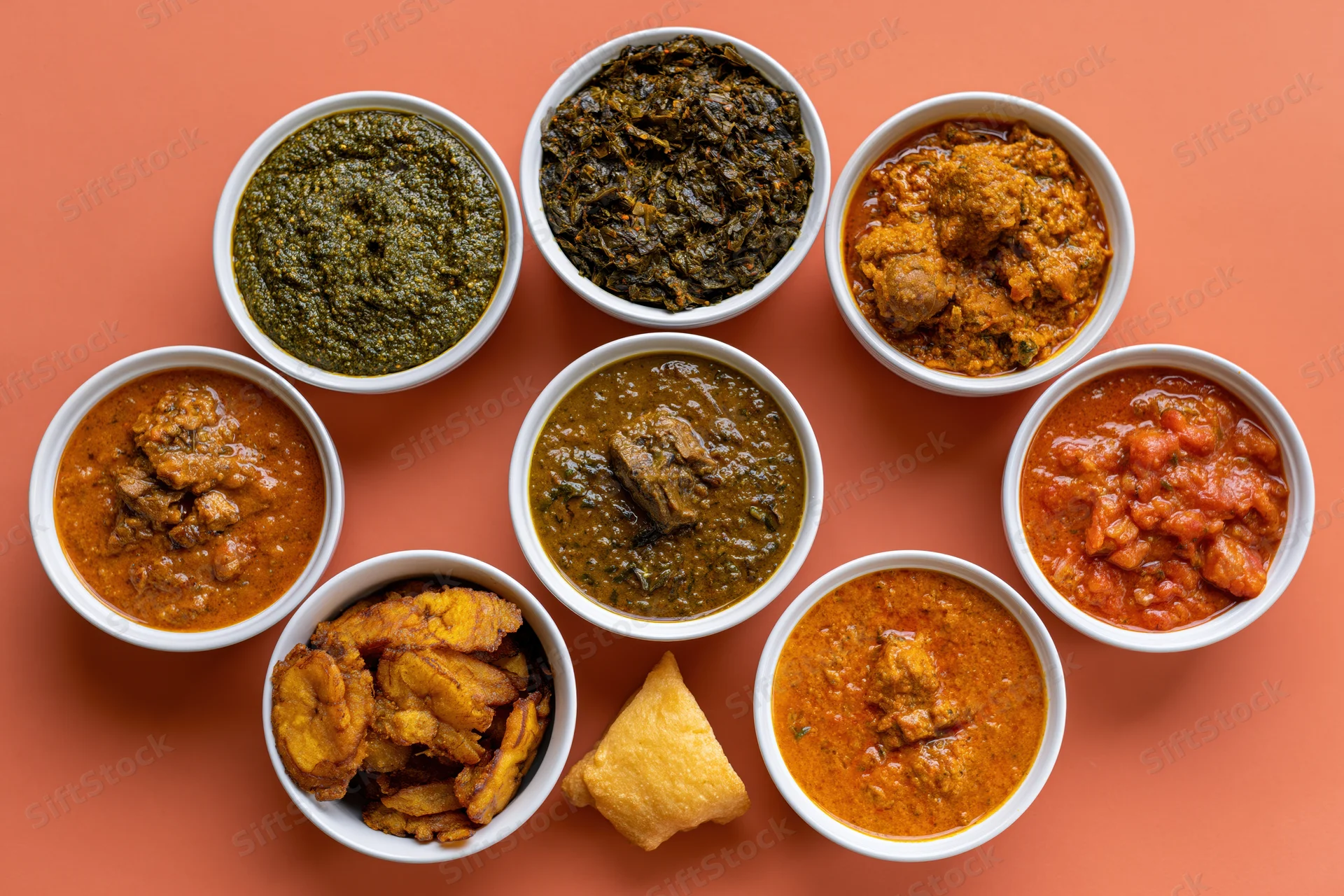 Nine white bowls of indian curries and sides arranged in a circle on orange surface