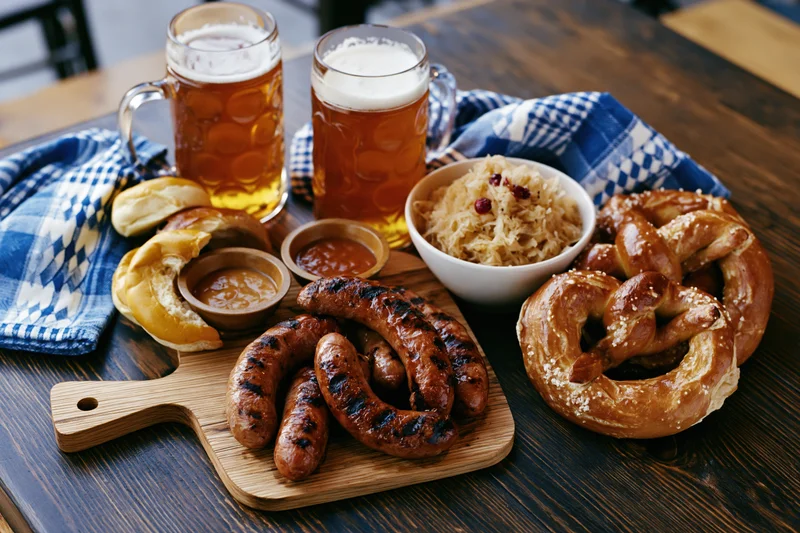 Oktoberfest food spread with grilled sausages, pretzels, sauerkraut, and beer on a wooden table