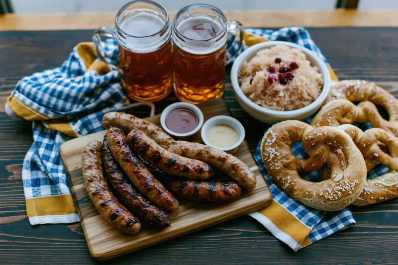 Grilled sausages, pretzels, and beer arranged on a wooden table with sauerkraut and condiments for an Oktoberfest spread