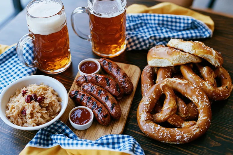 Oktoberfest food spread with beer, pretzels, sausages and sauerkraut on dark wooden table