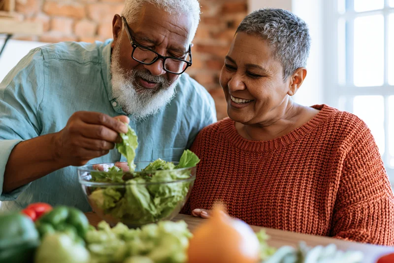 Senior couple preparing salad together at kitchen counter