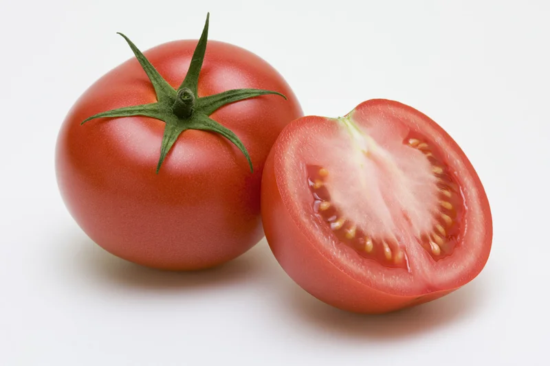 Whole ripe red tomato with green calyx next to a sliced half on white background
