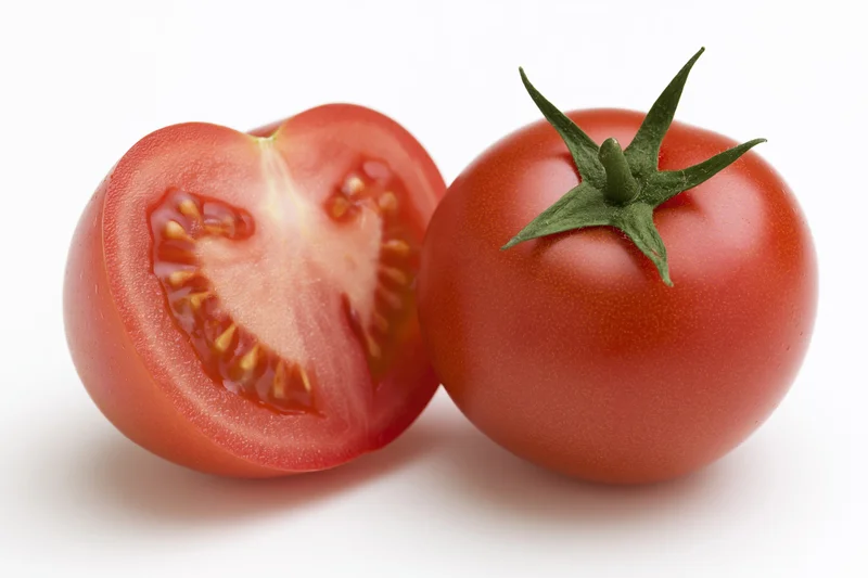 Whole and sliced red tomato with green calyx on white background