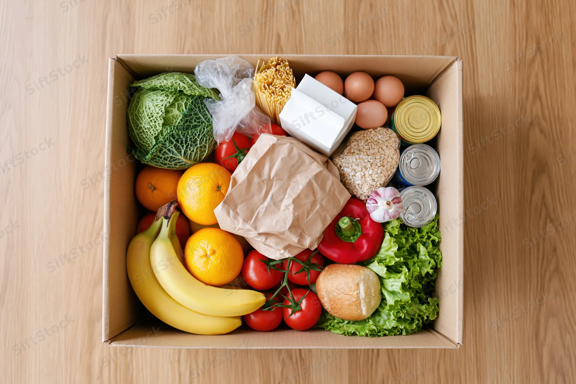 Open cardboard box filled with assorted groceries on wooden surface