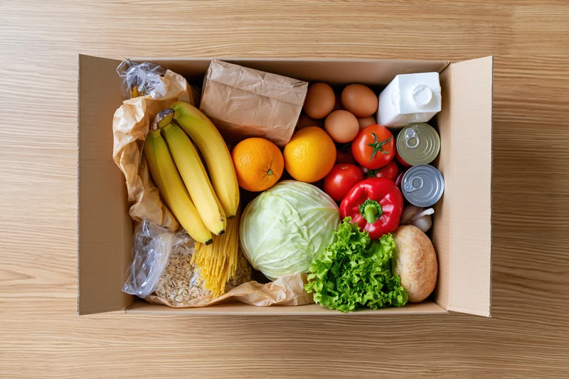 Open cardboard box filled with assorted groceries on wooden surface