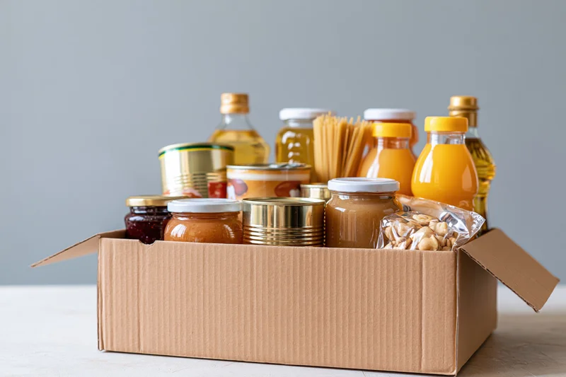 Open cardboard box filled with assorted pantry staples on a table
