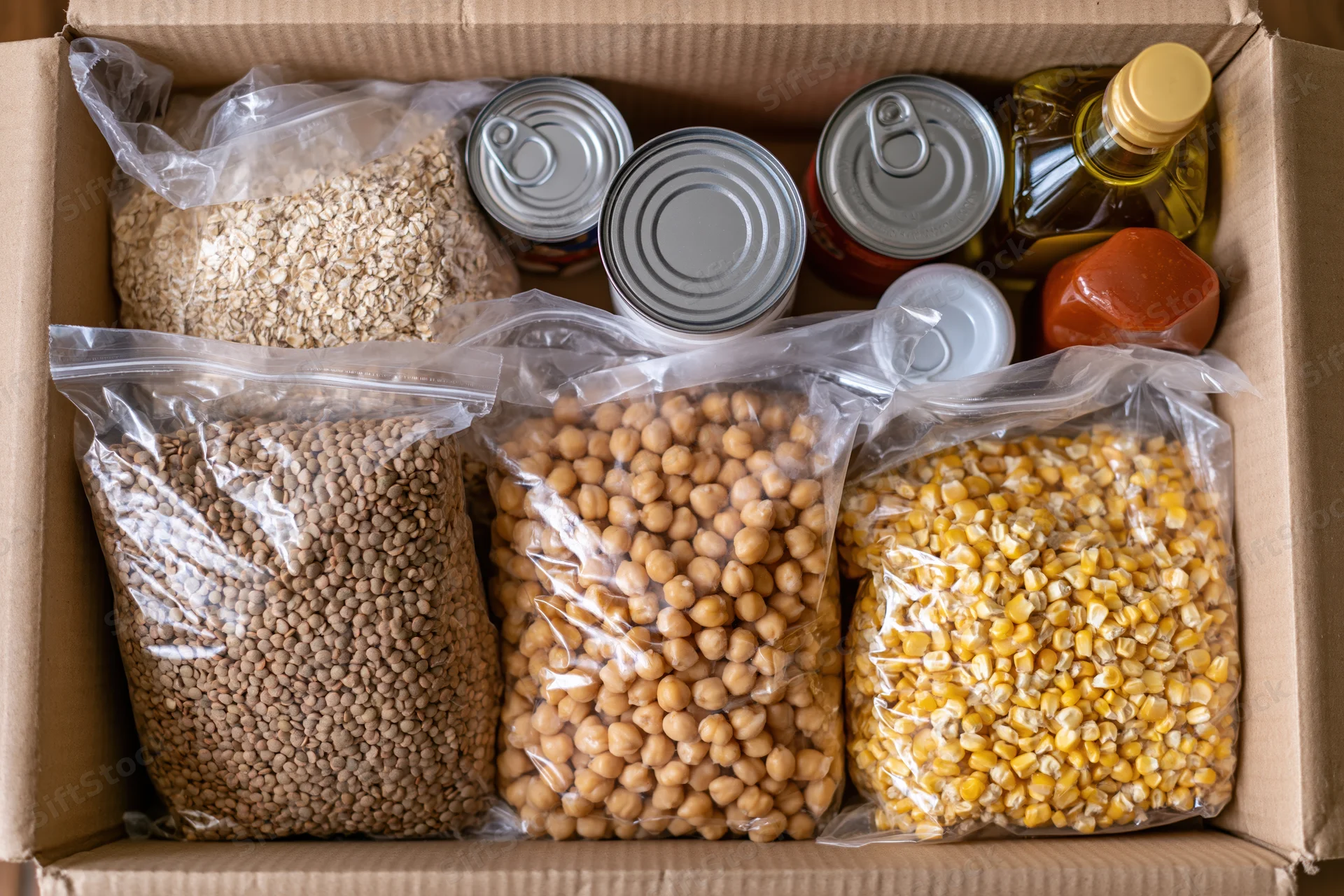 Open cardboard box filled with dry food donation items including grains legumes and canned goods