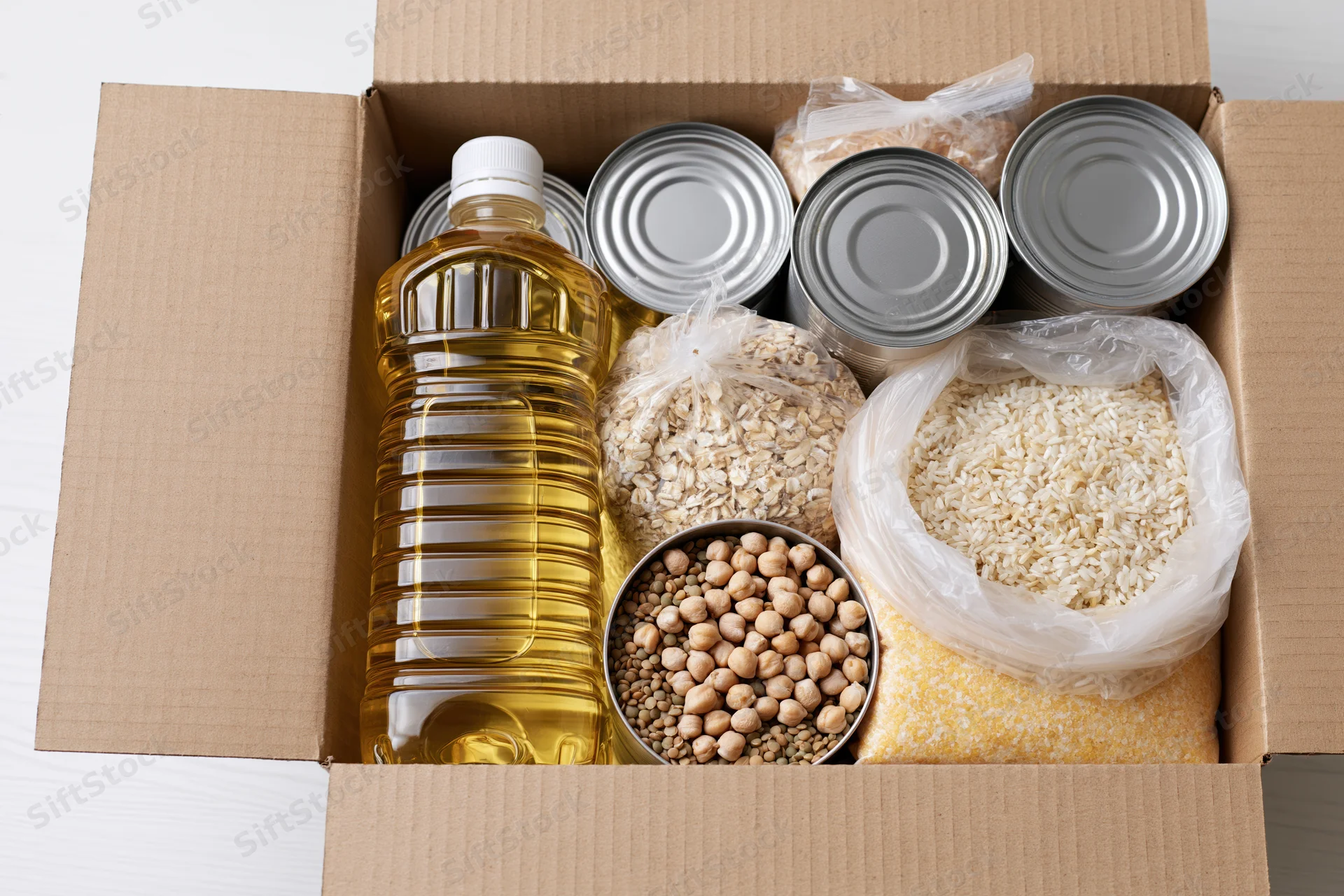 Open cardboard box filled with nonperishable food items including canned goods, rice, oats, beans, and cooking oil