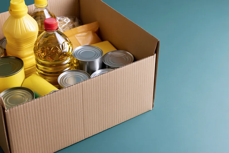Open cardboard box filled with canned goods and plastic bottles on a blue surface