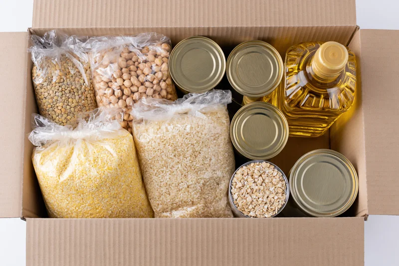Open cardboard box filled with dry food staples and canned goods for donation