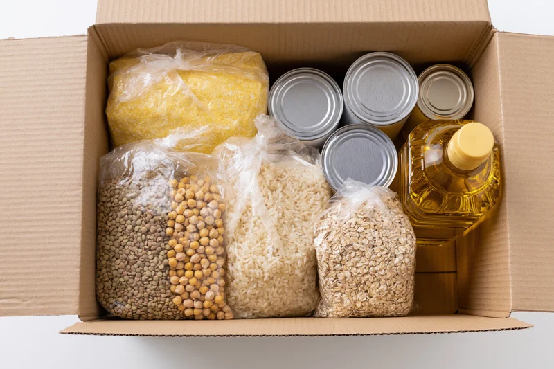 Open cardboard box filled with dry food staples and canned goods for donation