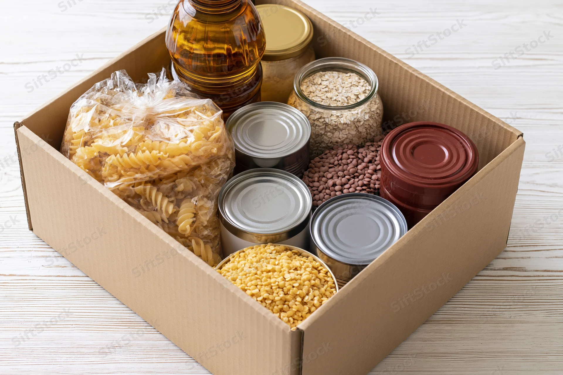 Open cardboard box filled with dry pantry goods on a wooden surface