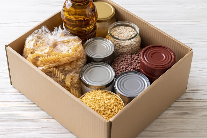 Open cardboard box filled with dry pantry goods on a wooden surface