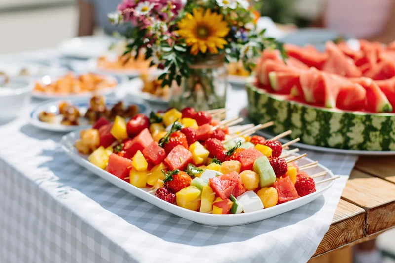Fruit skewers arranged on a white platter on a checkered tablecloth at an outdoor garden dining table