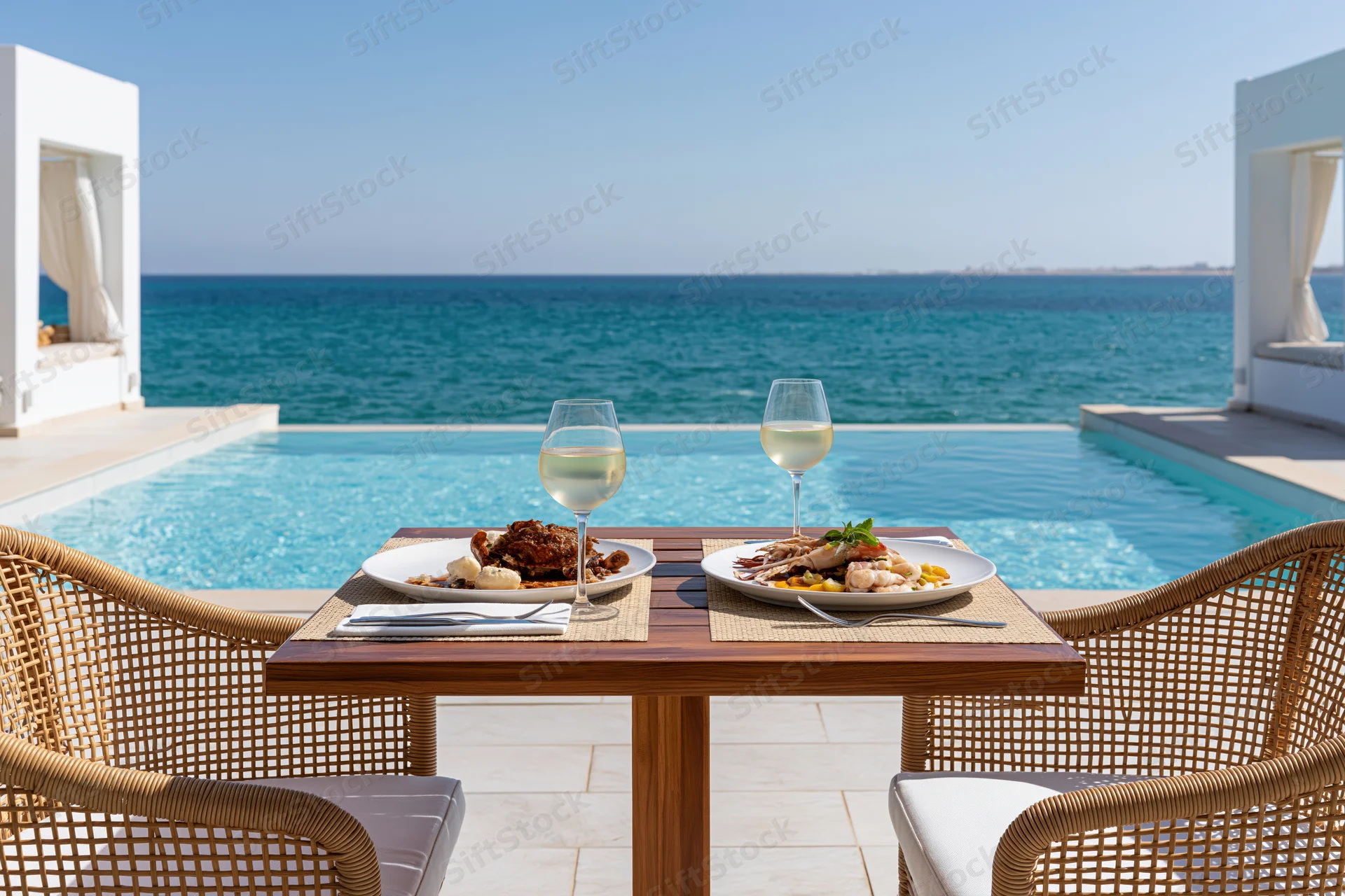 Dining table set for two with food and wine by a pool overlooking the ocean at a luxury beachfront resort
