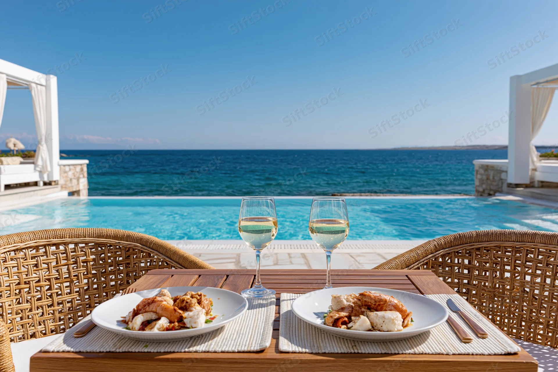 Dining table set for two with seafood and wine by a pool overlooking the ocean at a luxury beachfront resort