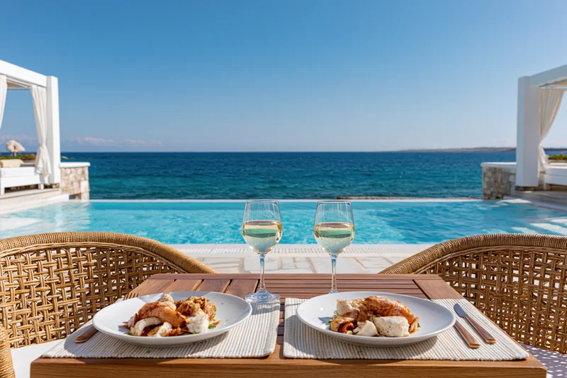 Dining table set for two with seafood and wine by a pool overlooking the ocean at a luxury beachfront resort