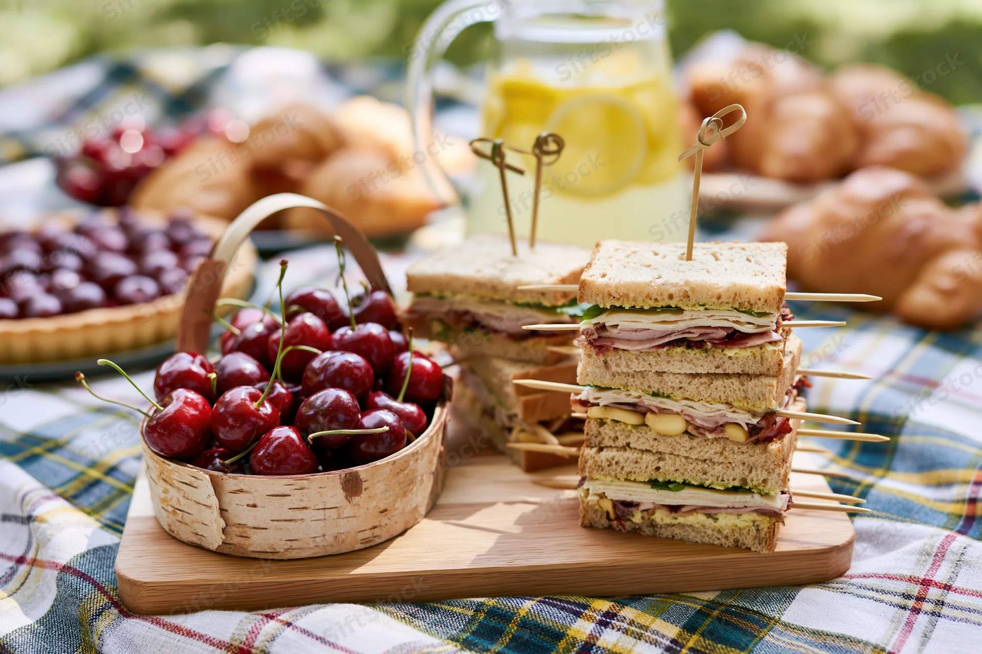 Picnic spread with sandwiches and cherries on a plaid blanket outdoors