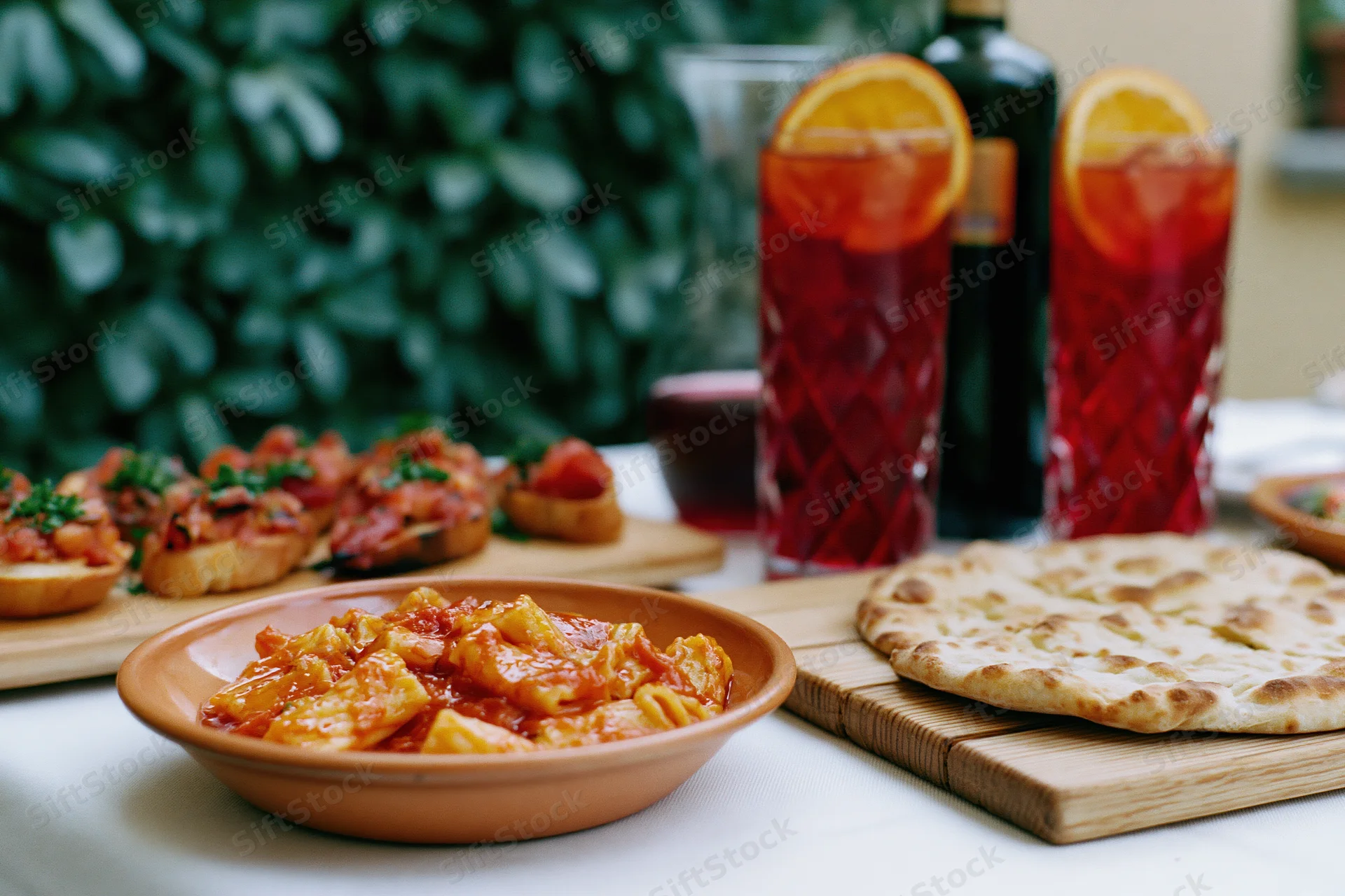 Pasta dish with tomato sauce and cheese in terracotta bowl on outdoor dining table with bruschetta and flatbread nearby