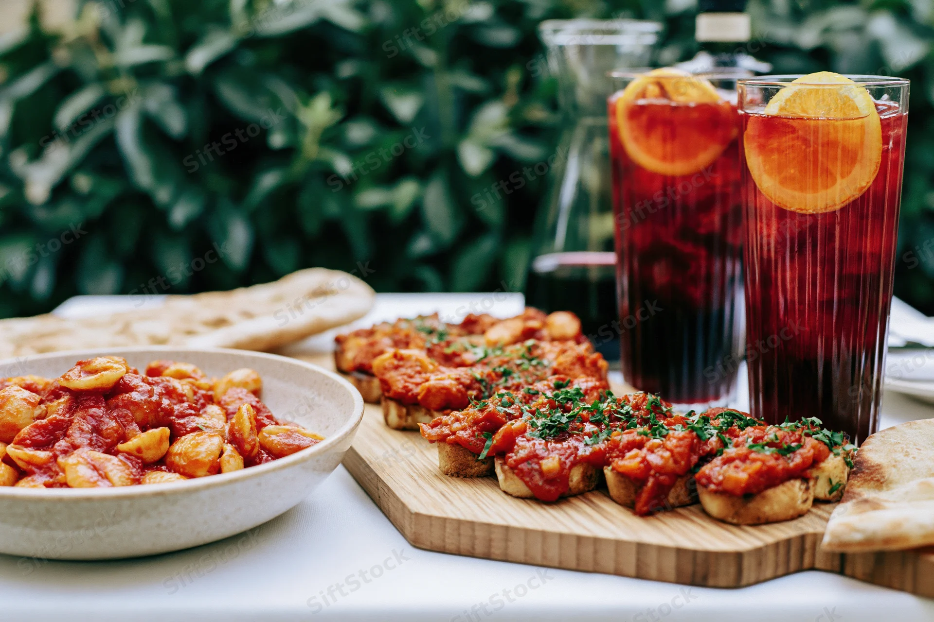 Pasta dish and bruschetta served on a table with drinks and greenery in the background
