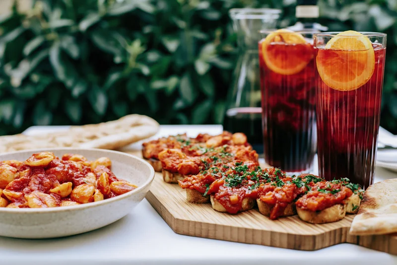 Pasta dish and bruschetta served on a table with drinks and greenery in the background