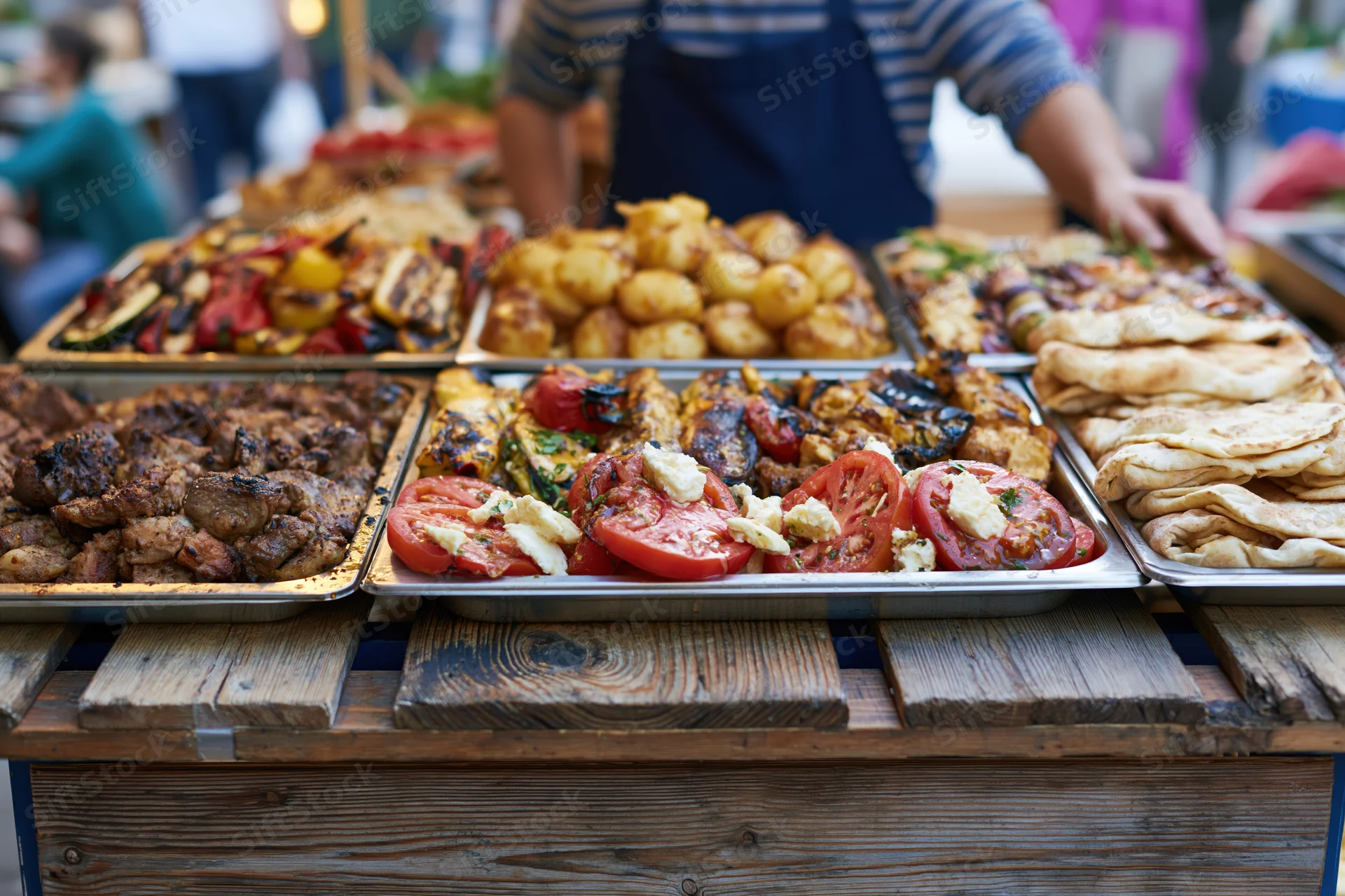 Street food vendor serving grilled meats and vegetables on metal trays at a rustic wooden stall