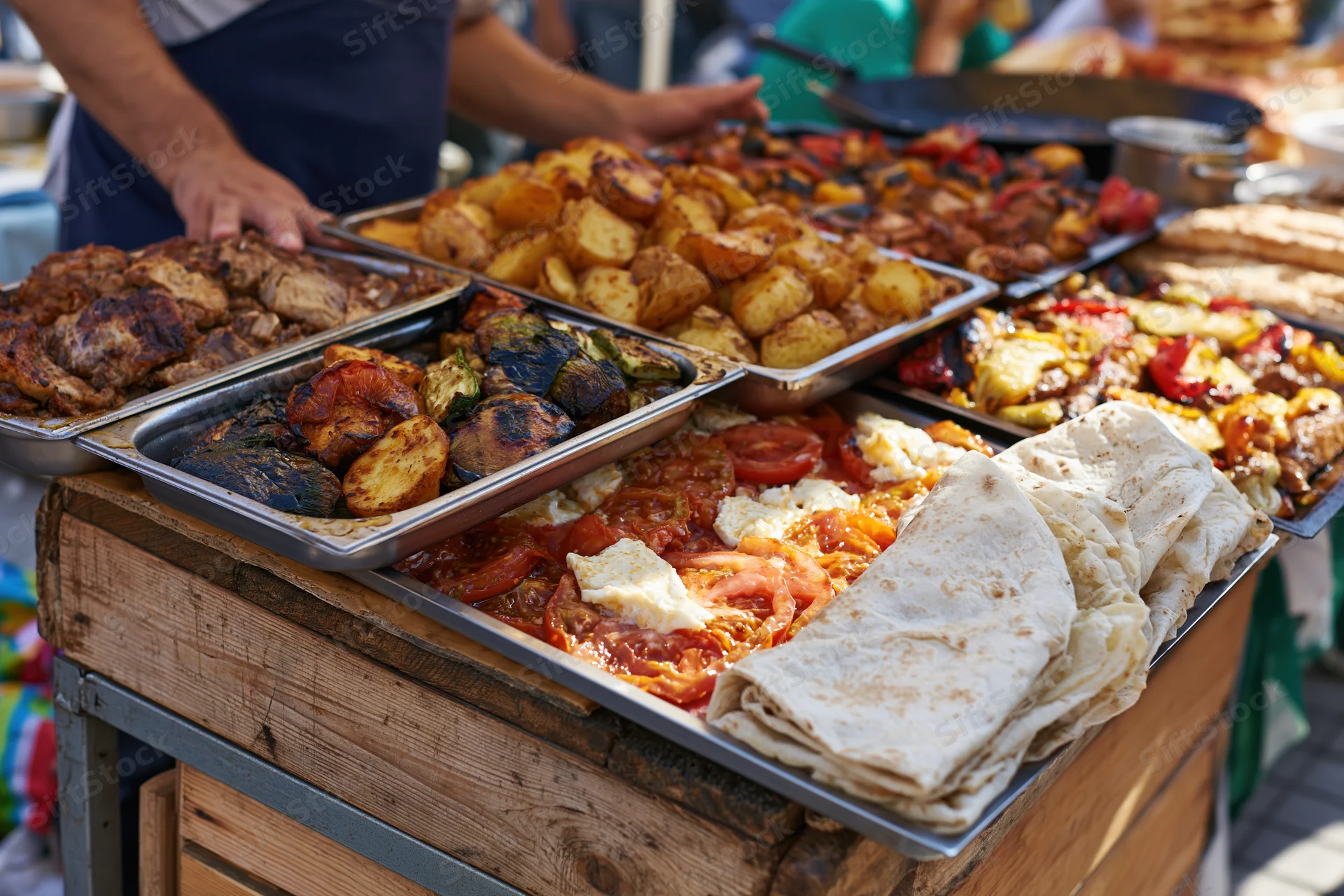 Street food vendor serving grilled meats and vegetables on metal trays at a wooden outdoor stall